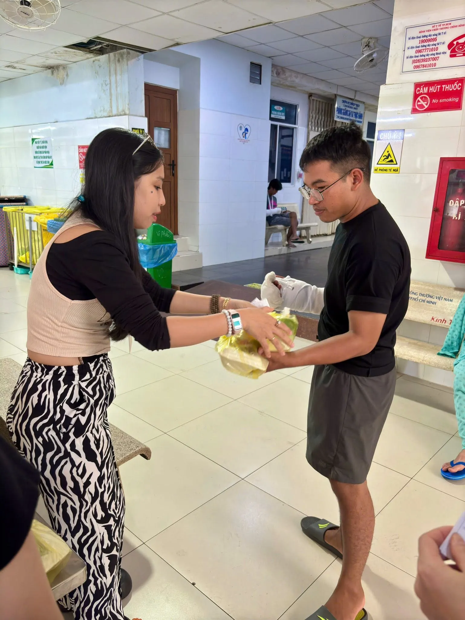 Tình nguyện viên trao phần cơm cho một người bó bột tay tại hành lang Bệnh viện Chấn Thương Chỉnh Hình