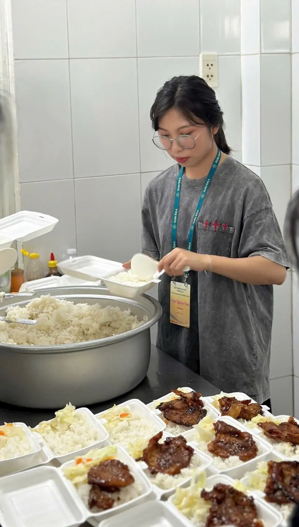 Một bạn tình nguyện viên bên nồi cơm lớn và những hộp xốp đã có cơm và thức ăn