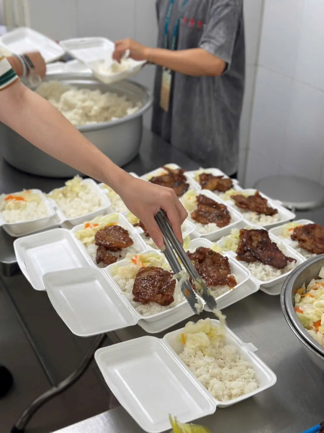 Cận cảnh tay gắp thức ăn vào những hộp cơm xốp xếp thành hàng