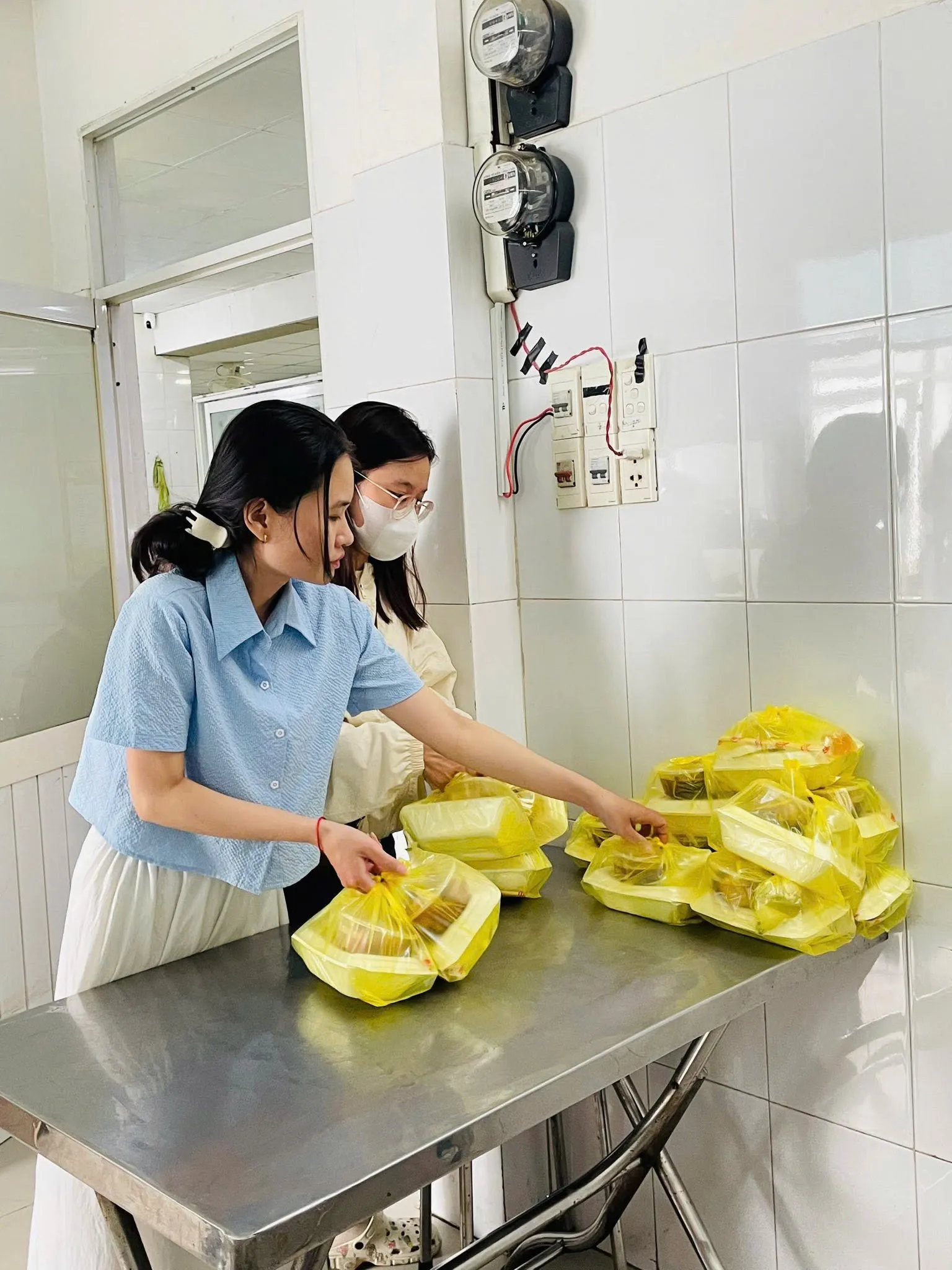 两位志愿者在不锈钢桌上整理袋装餐食