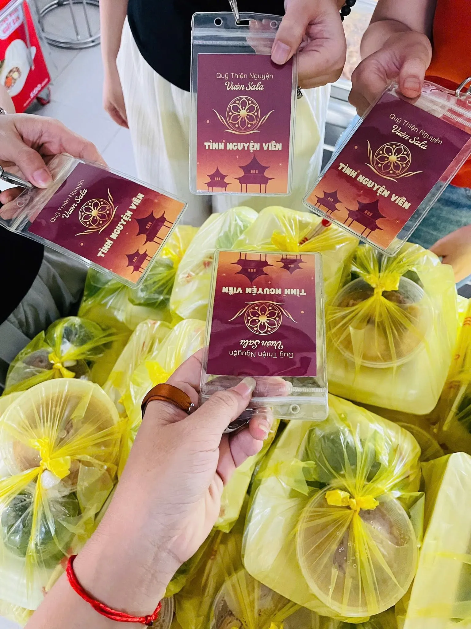 Bốn tấm thẻ Quỹ Thiện Nguyện Vườn Sala – Tình nguyện viên được giơ lên trên những túi phần ăn màu vàng