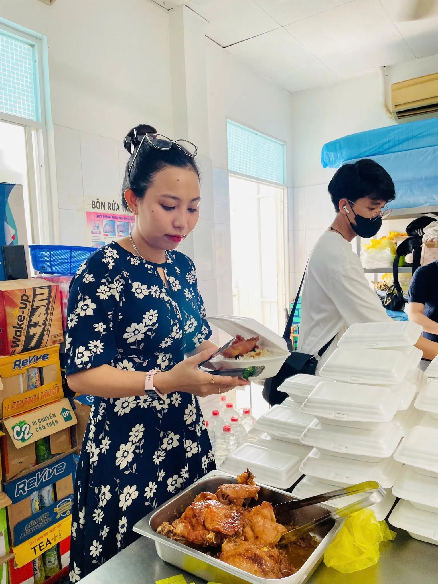 一位志愿者手拿饭盒，旁边是一盘菜和一摞泡沫餐盒