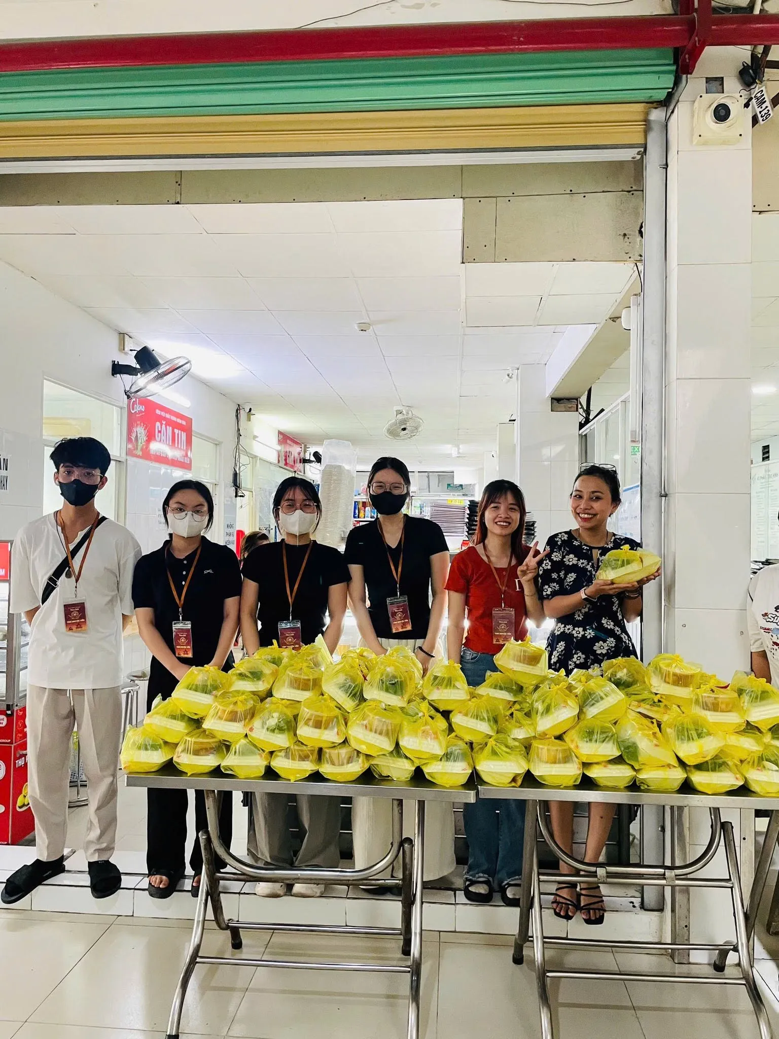 志愿者们站在食堂前两张摆满餐袋的桌子后面