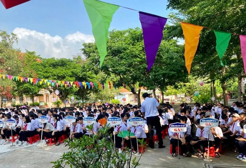 年终总结典礼上，各班学生坐在树荫下，校园里挂满彩旗