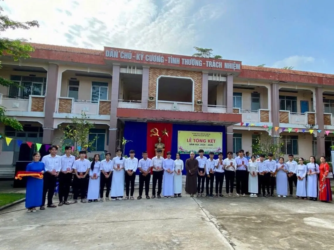获得奖学金的学生与法师及来宾们在写有“Dân chủ – Kỷ cương – Tình thương – Trách nhiệm”（民主—纪律—仁爱—责任）标语的教学楼前合影留念