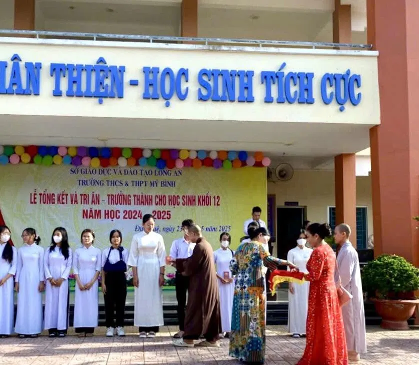 Vị Thầy áo nâu trao quà cho học sinh trước phông Lễ Tổng kết và Tri ân – Trưởng thành cho học sinh khối 12, năm học 2024 – 2025 của Trường THCS & THPT Mỹ Bình