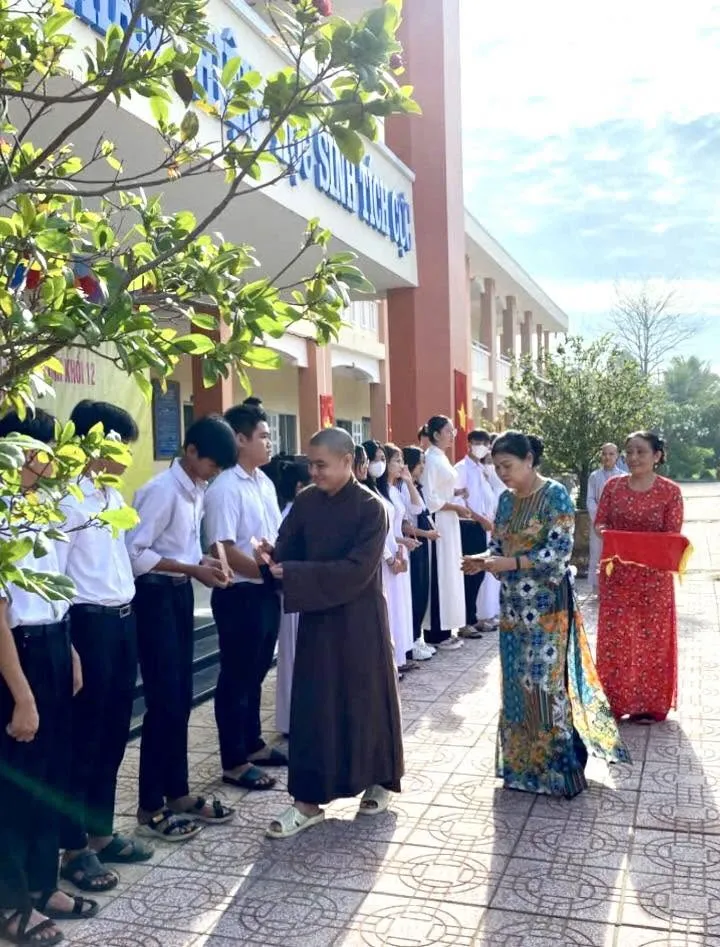 身穿褐色僧袍的法师在校园里把礼物逐一交到排队的学生手中
