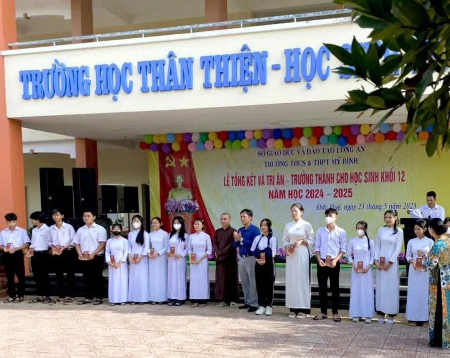 学生们手持礼物，与身穿褐色僧袍的法师站在2024–2025学年总结典礼背景板前（Đức Huệ，2025年5月23日）