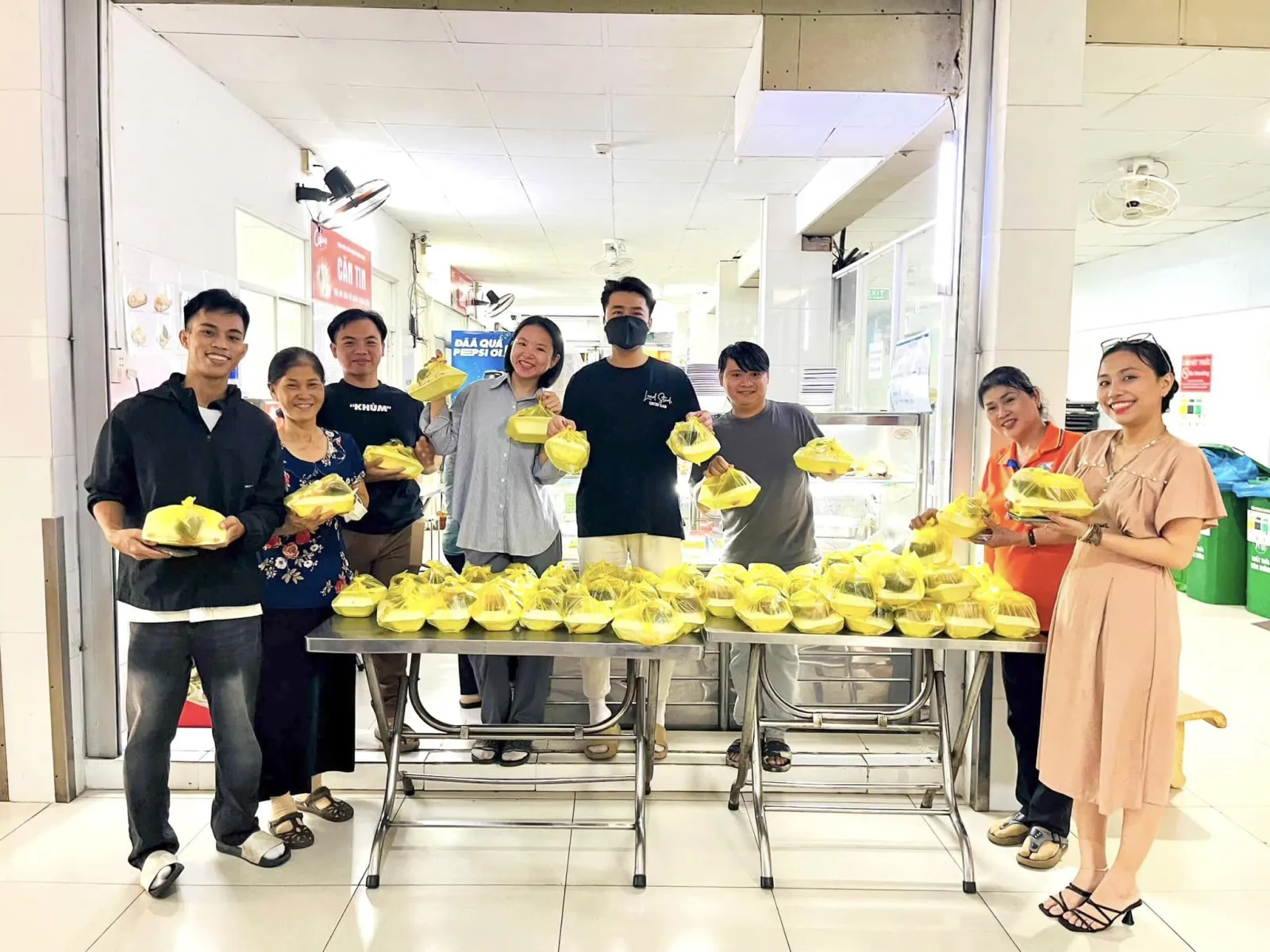Các bạn tình nguyện viên Vườn Sala tươi cười cầm những phần ăn trưa bên dãy bàn trong căn tin bệnh viện