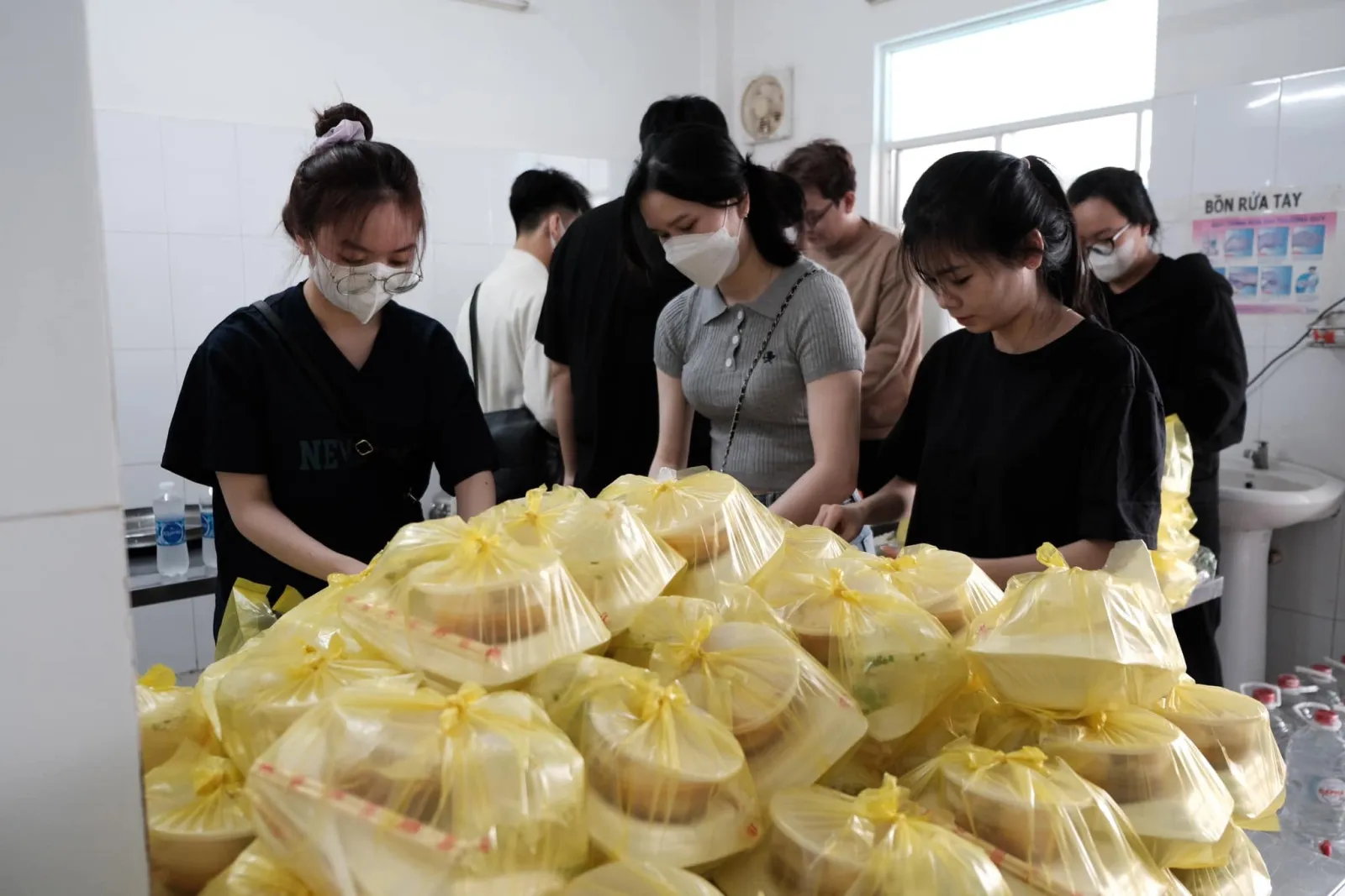 Các bạn tình nguyện viên đóng gói bên bàn chất đầy những túi phần ăn màu vàng