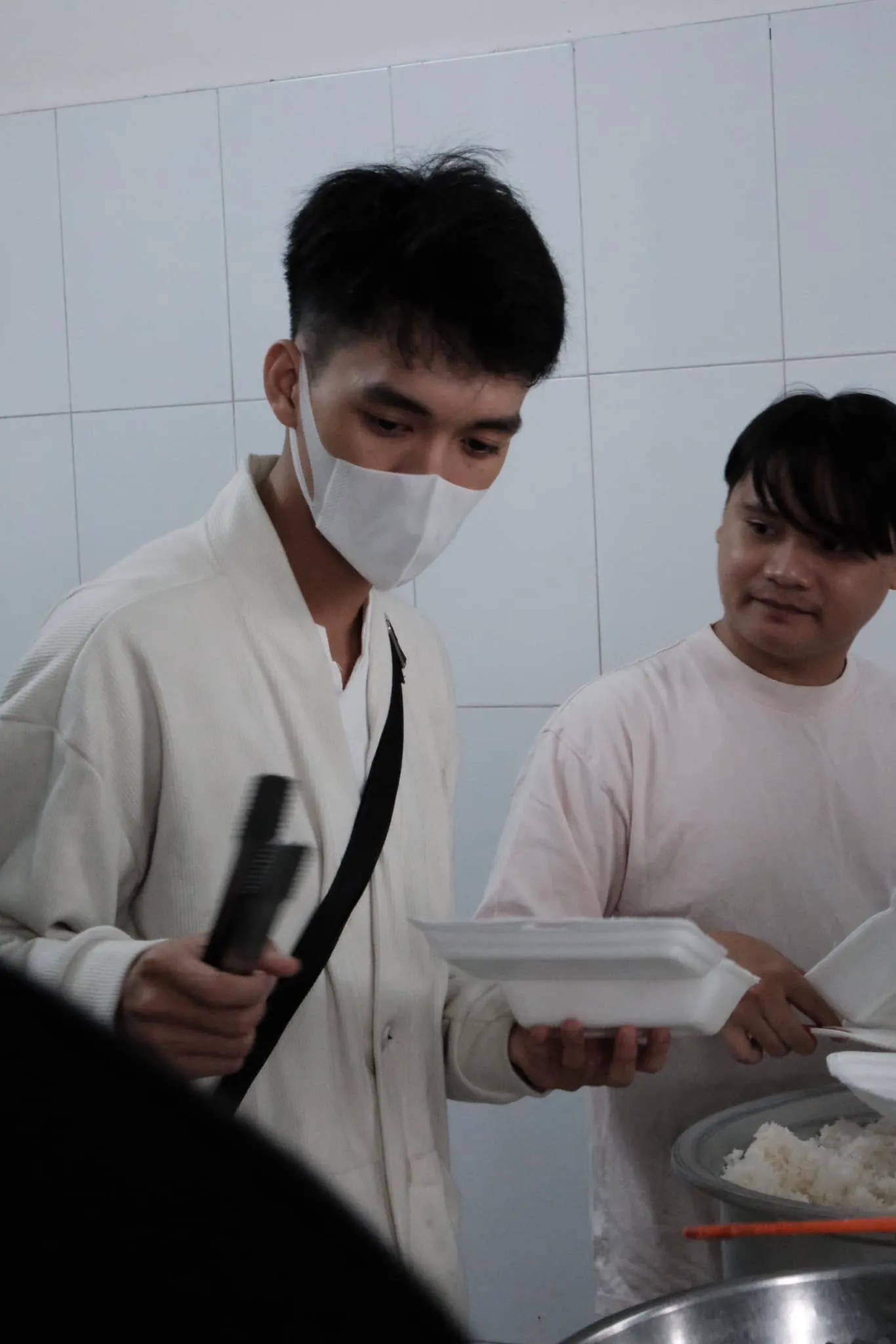 一位志愿者用夹子把菜夹进泡沫餐盒