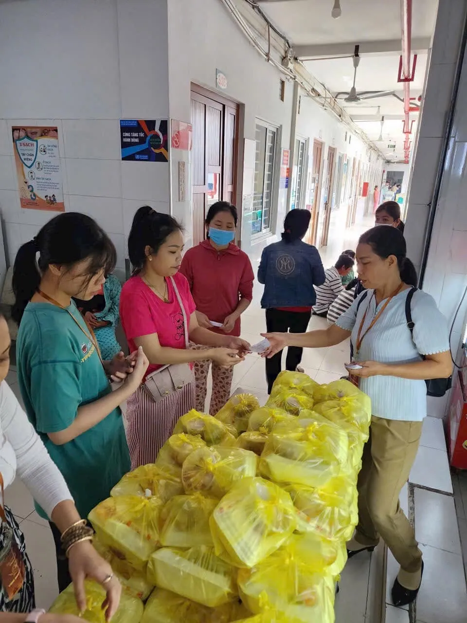 志愿者们在医院走廊摆满黄色袋子的桌旁向人们分发午餐