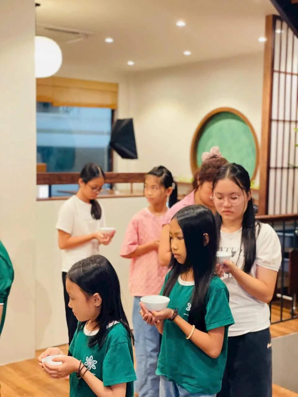 Các em nhỏ và người lớn đứng thành hàng, hai tay nâng chén trà