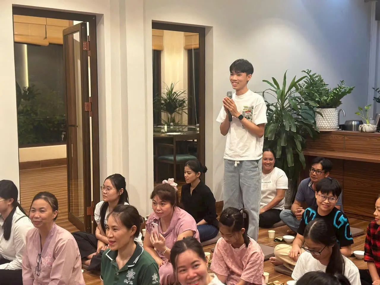 Một bạn trẻ đứng chắp tay cầm micro chia sẻ giữa những người đang ngồi