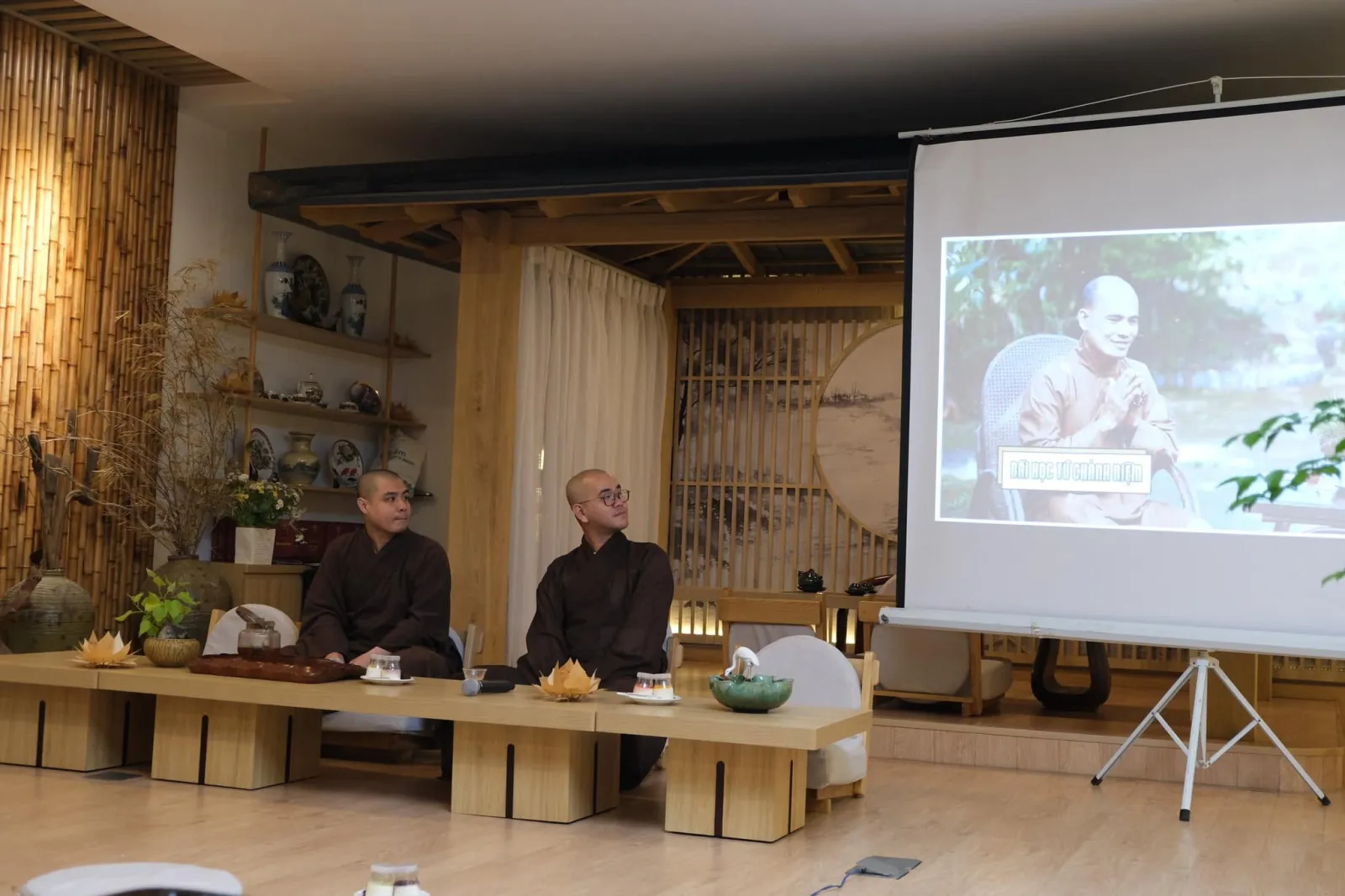 The screen showing a monk with the caption “Bài học từ chánh niệm” (Lessons from mindfulness), two monks seated beside it