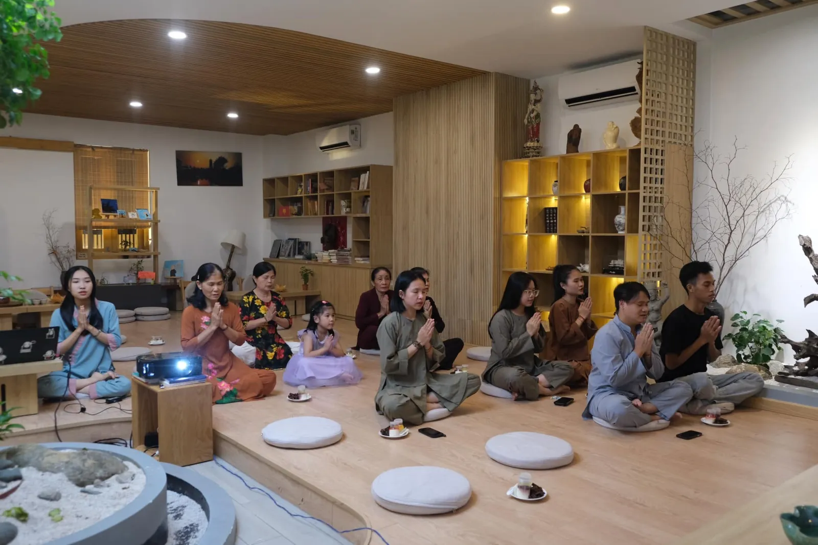 Members sitting on meditation cushions, listening with joined palms