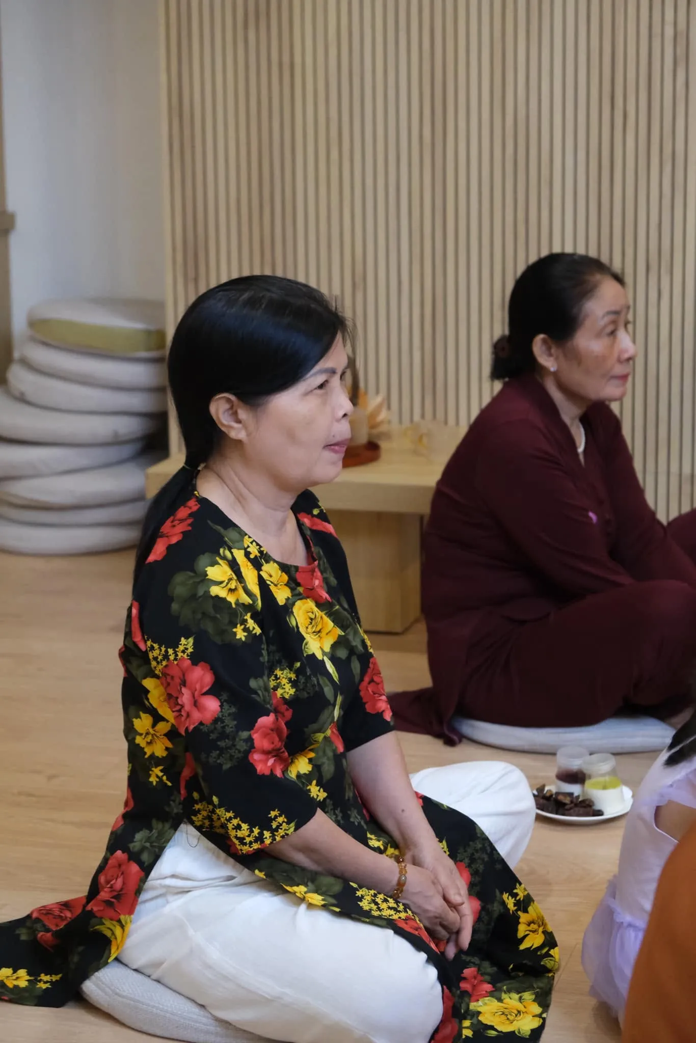 Two women sitting on cushions, listening attentively