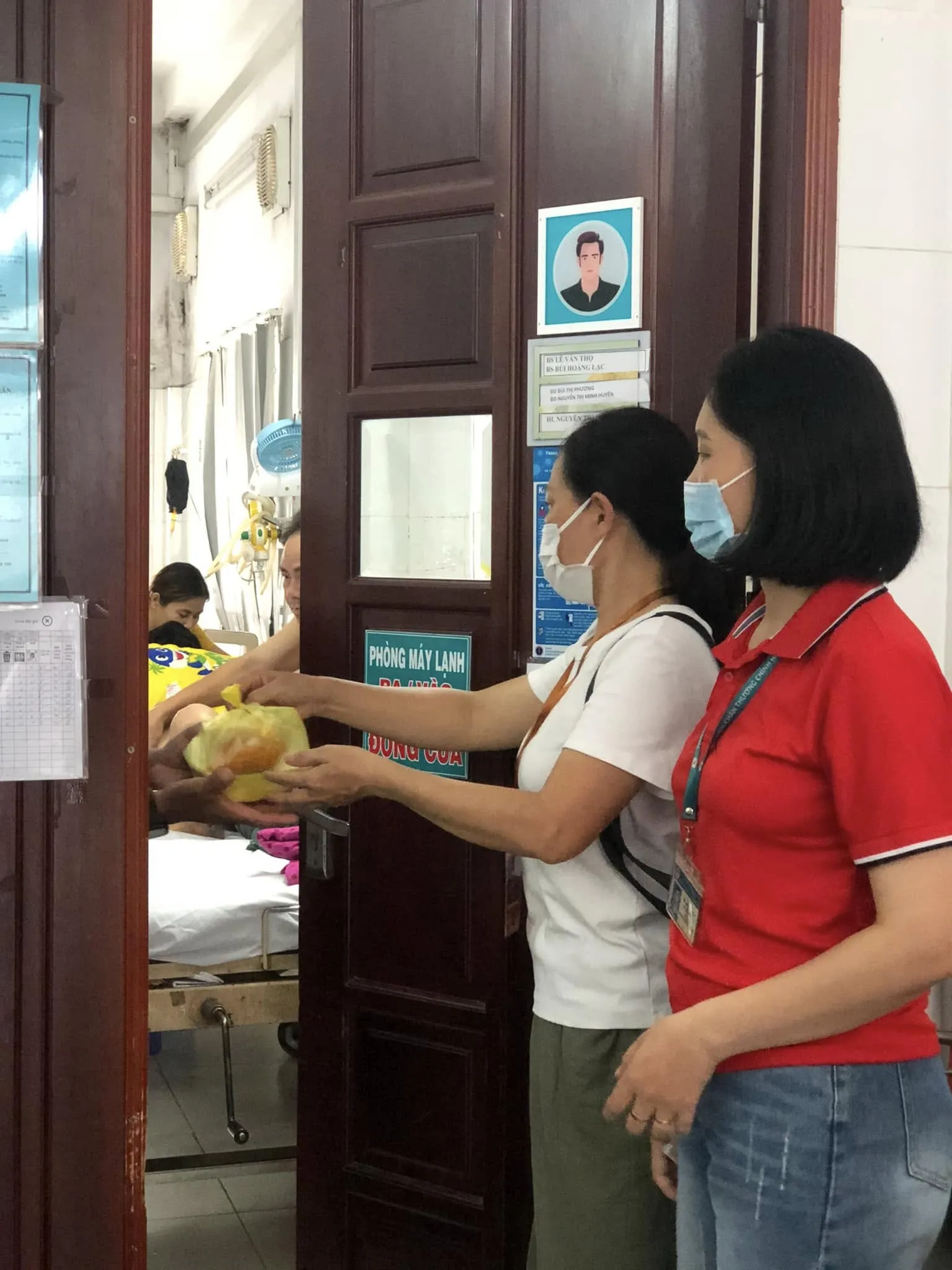 Hai cô đeo khẩu trang trao phần ăn trong túi vàng cho người bên trong phòng bệnh