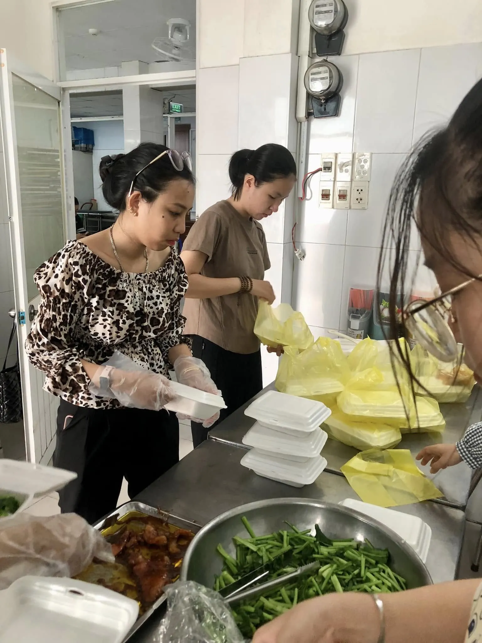 戴着手套的志愿者们把饭菜分装进泡沫餐盒,旁边是一盆青菜