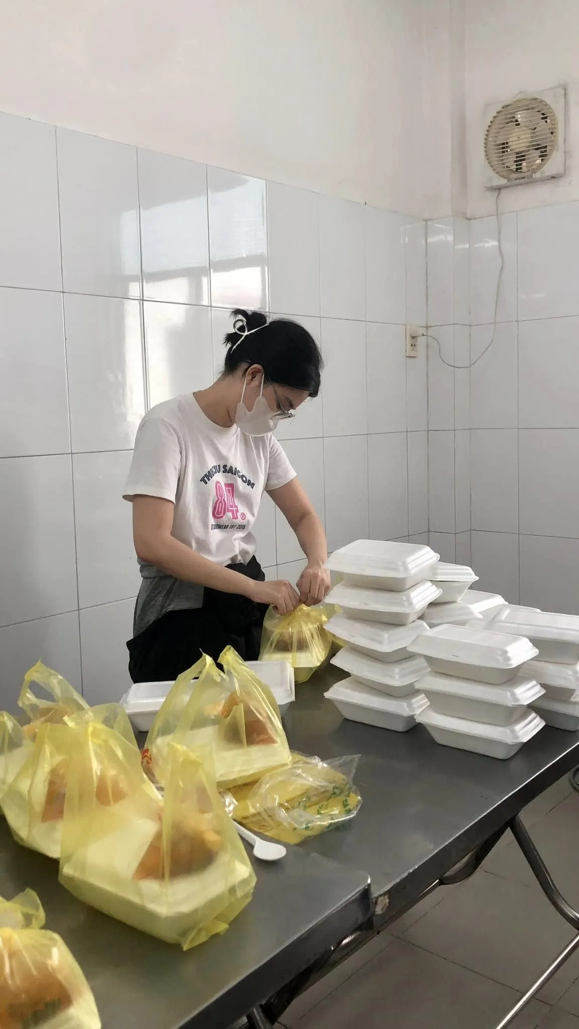 一位志愿者在不锈钢台上的一摞泡沫餐盒旁打包餐食
