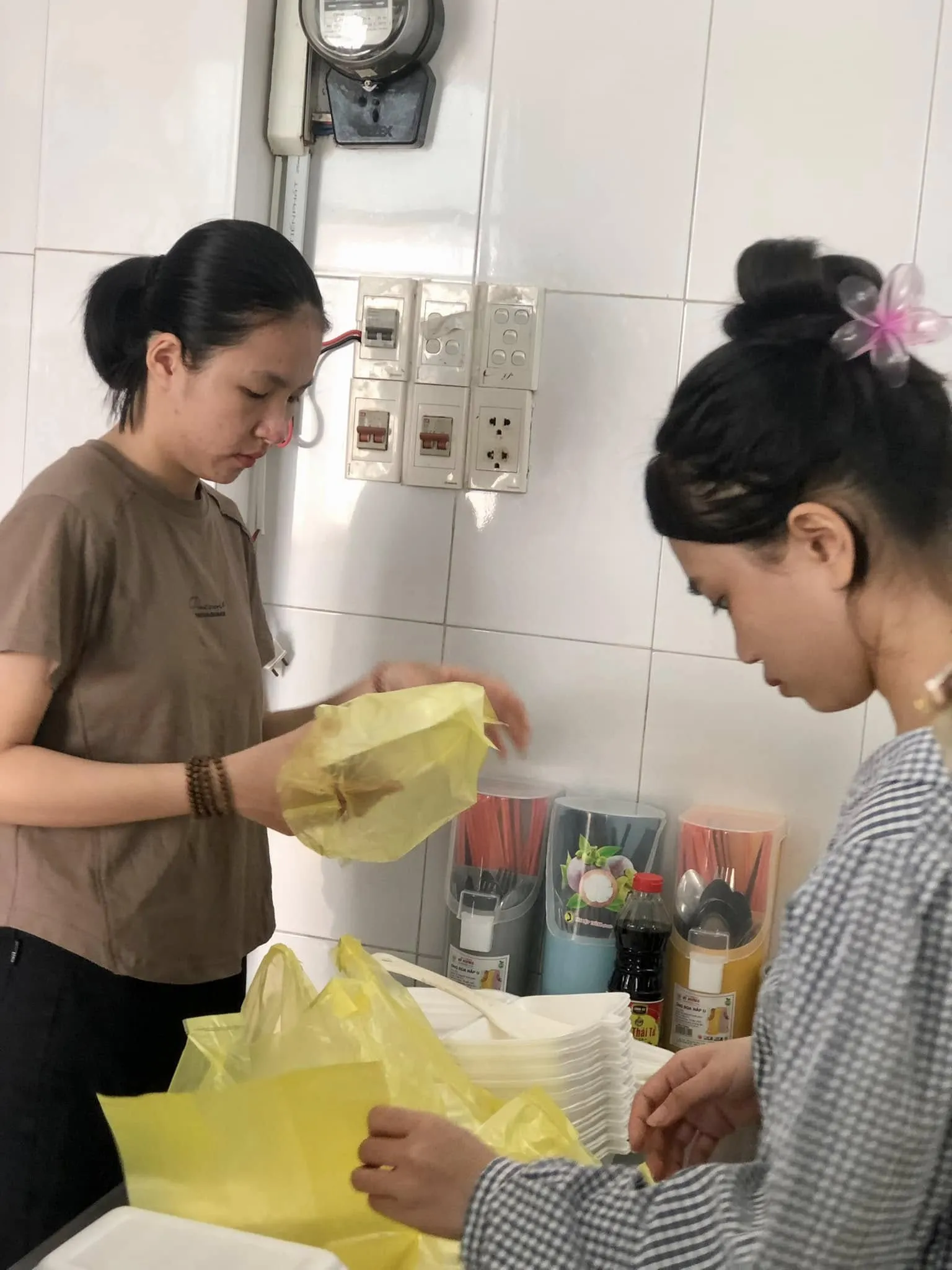 两位志愿者撑开黄色袋子装餐食