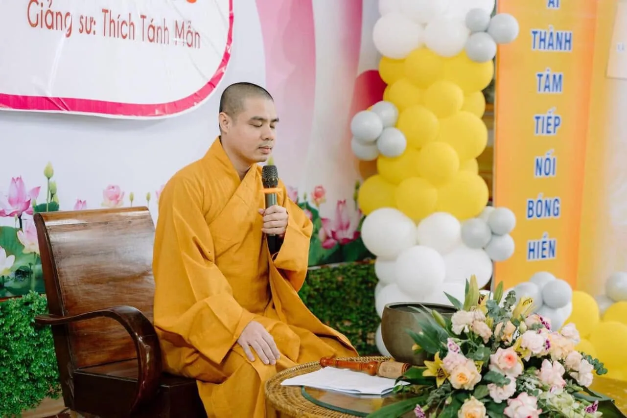 The Dharma teacher seated and speaking beside the backdrop reading “Giảng sư: Thích Tánh Mẫn”