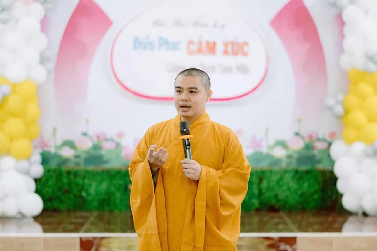 The Dharma teacher standing with a microphone in front of the “Điều phục cảm xúc” backdrop