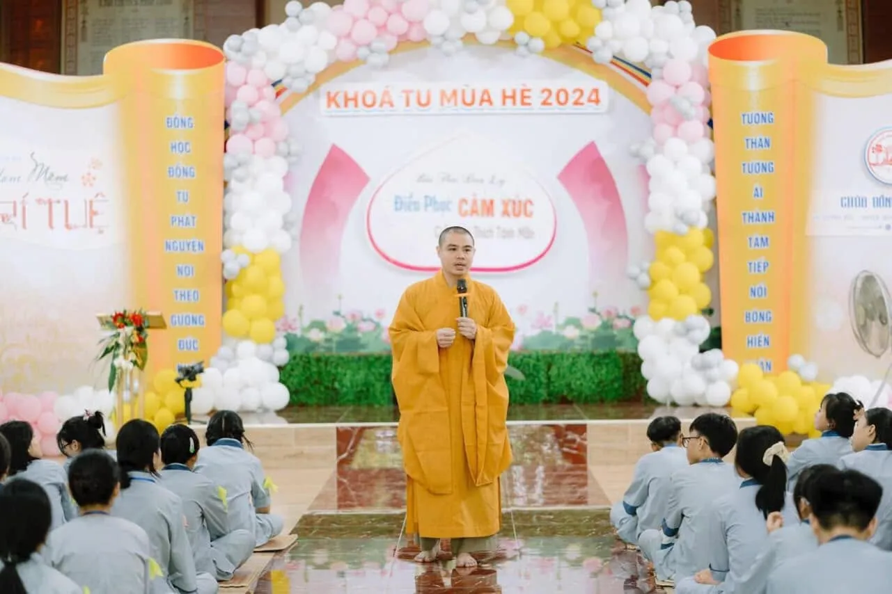 The Dharma teacher speaking on the 2024 Summer Retreat stage, with retreatants seated in front listening