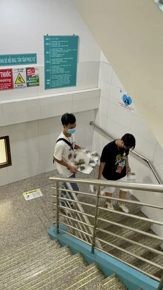 两位戴口罩的志愿者提着餐袋走下医院楼梯