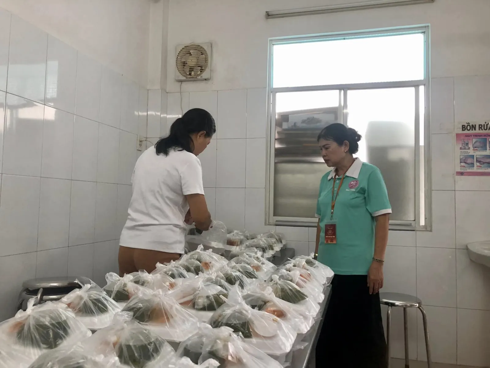 两位志愿者在不锈钢桌上整理一袋袋餐食