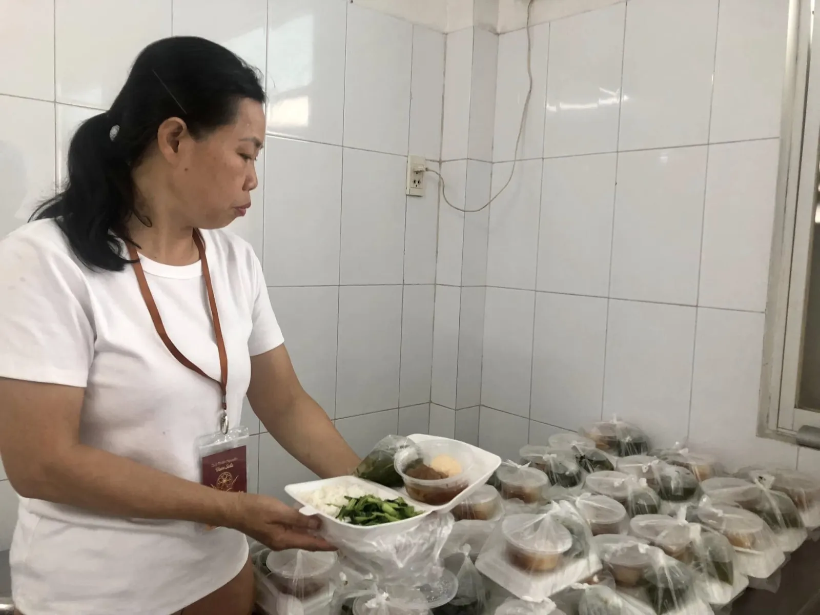 一位志愿者手捧装有青菜的泡沫餐盒,旁边是一袋袋餐食