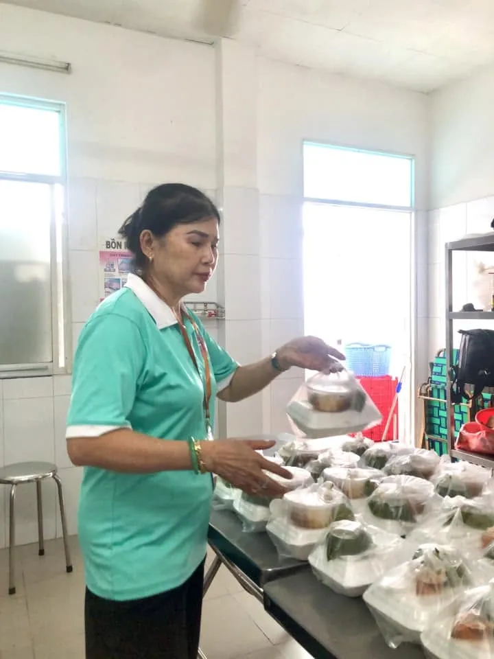 一位身穿青绿色上衣的志愿者在桌旁拿着一袋餐食