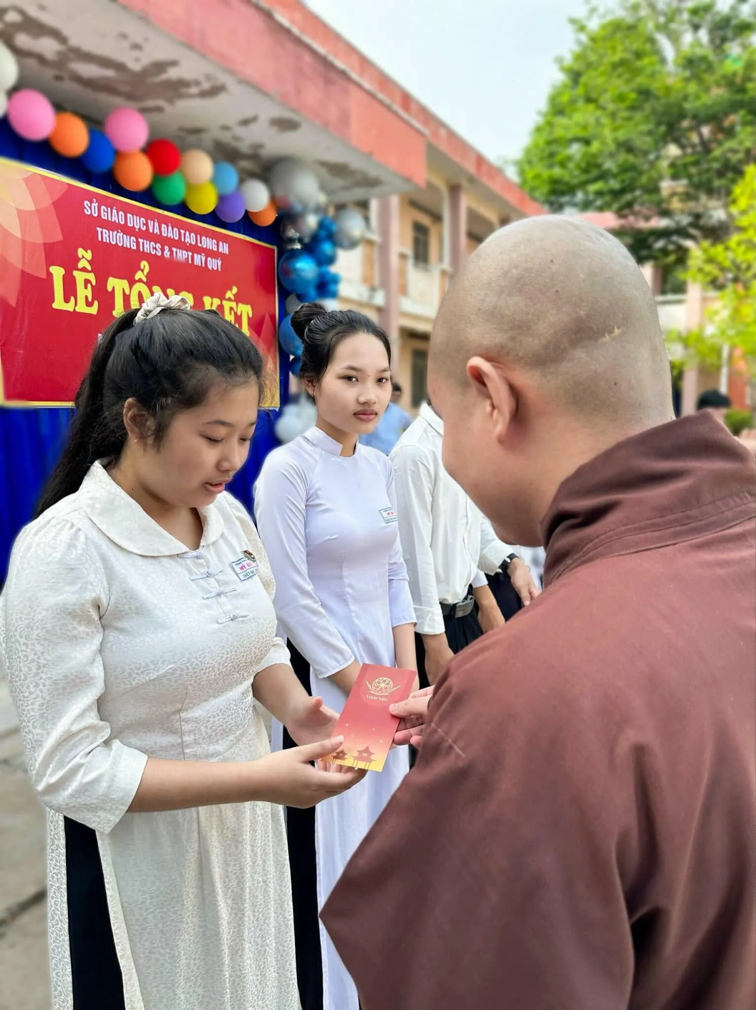 Vị thầy mặc áo nâu trao phong bì học bổng cho một em học sinh nữ tại Trường THCS & THPT Mỹ Quý