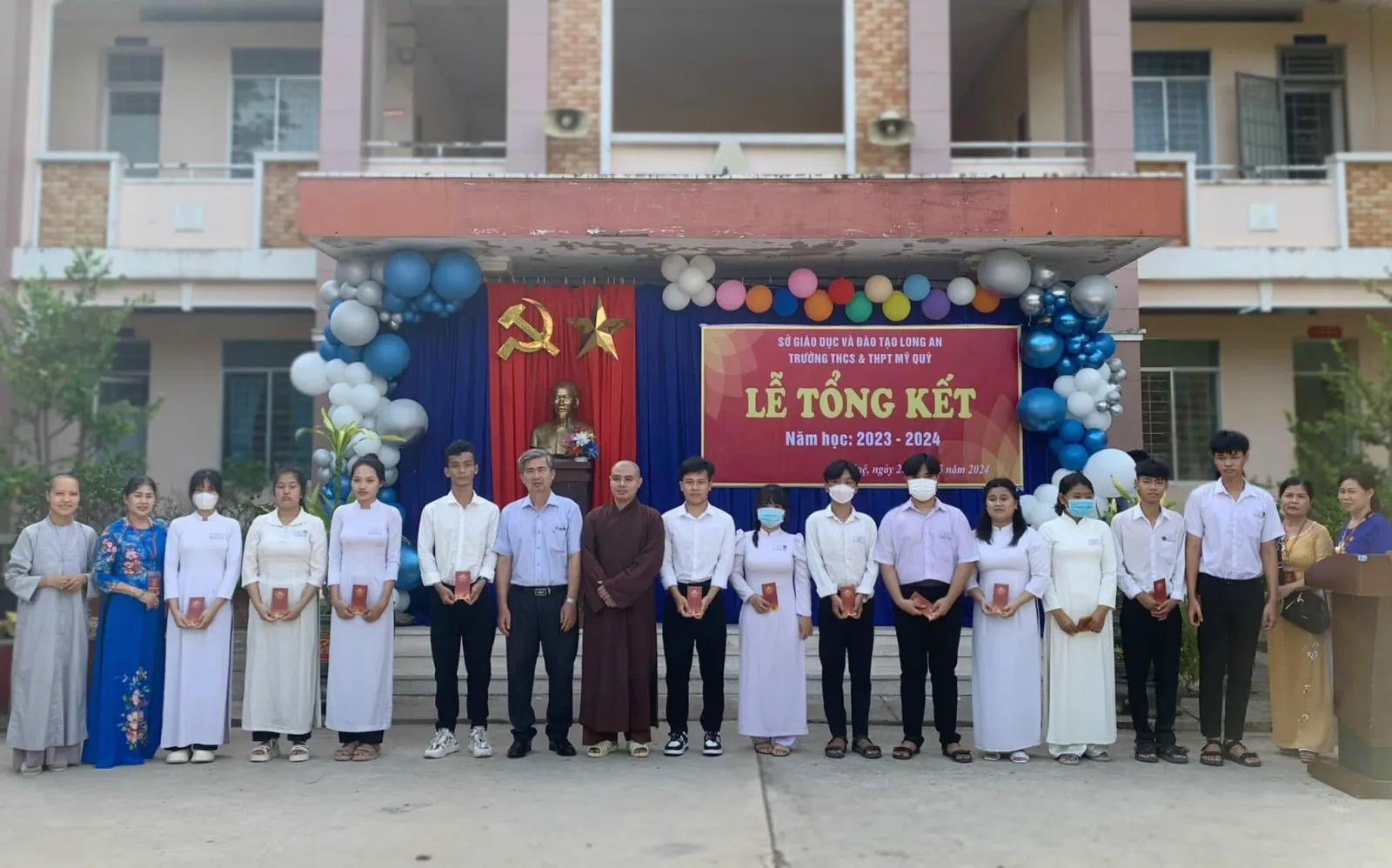 在 Trường THCS & THPT Mỹ Quý 2023–2024学年总结典礼背景板前与获奖学生合影