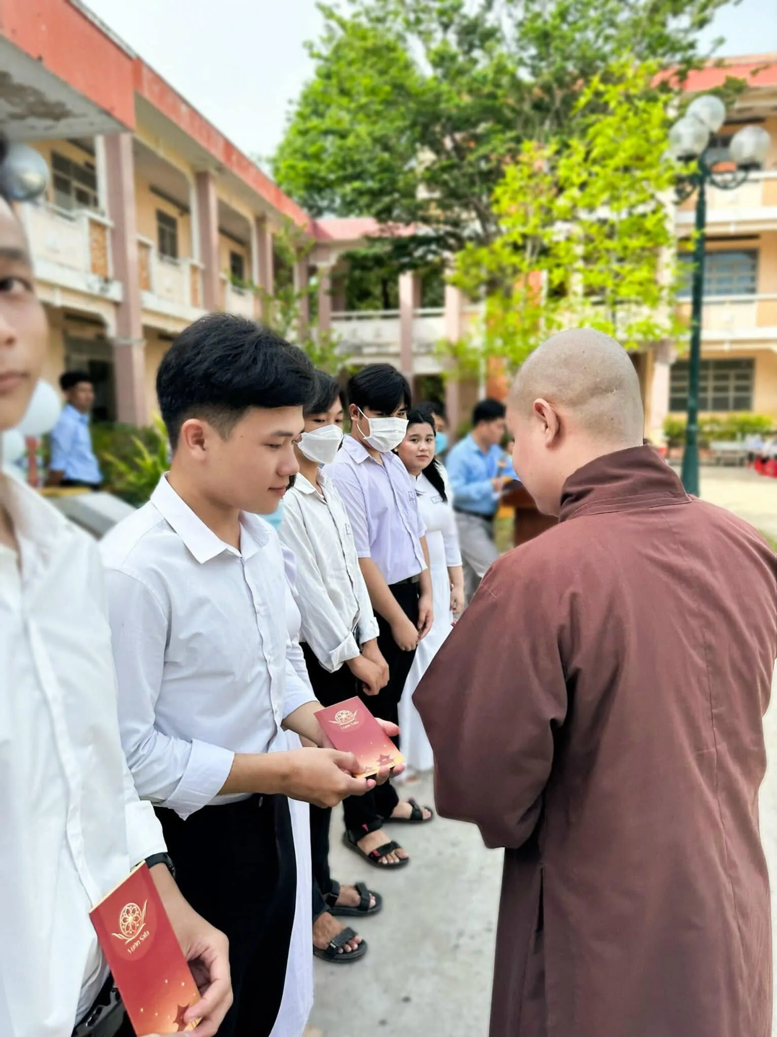身着褐色僧袍的法师向一名男学生颁发奖学金红包