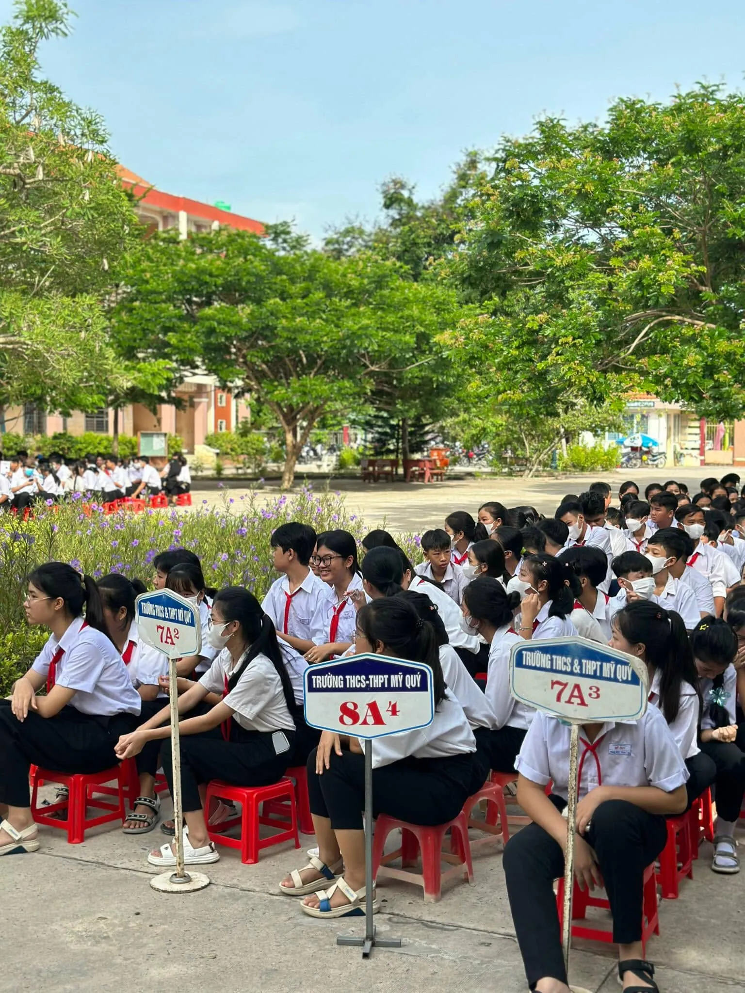 Trường THCS & THPT Mỹ Quý 的学生们按班级坐在树荫下参加总结典礼