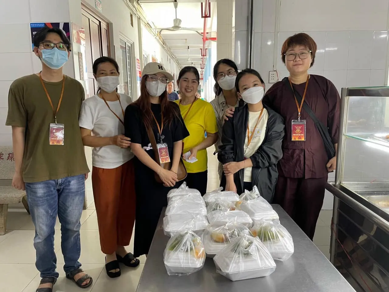 志愿者们站在摆满餐袋的不锈钢桌旁