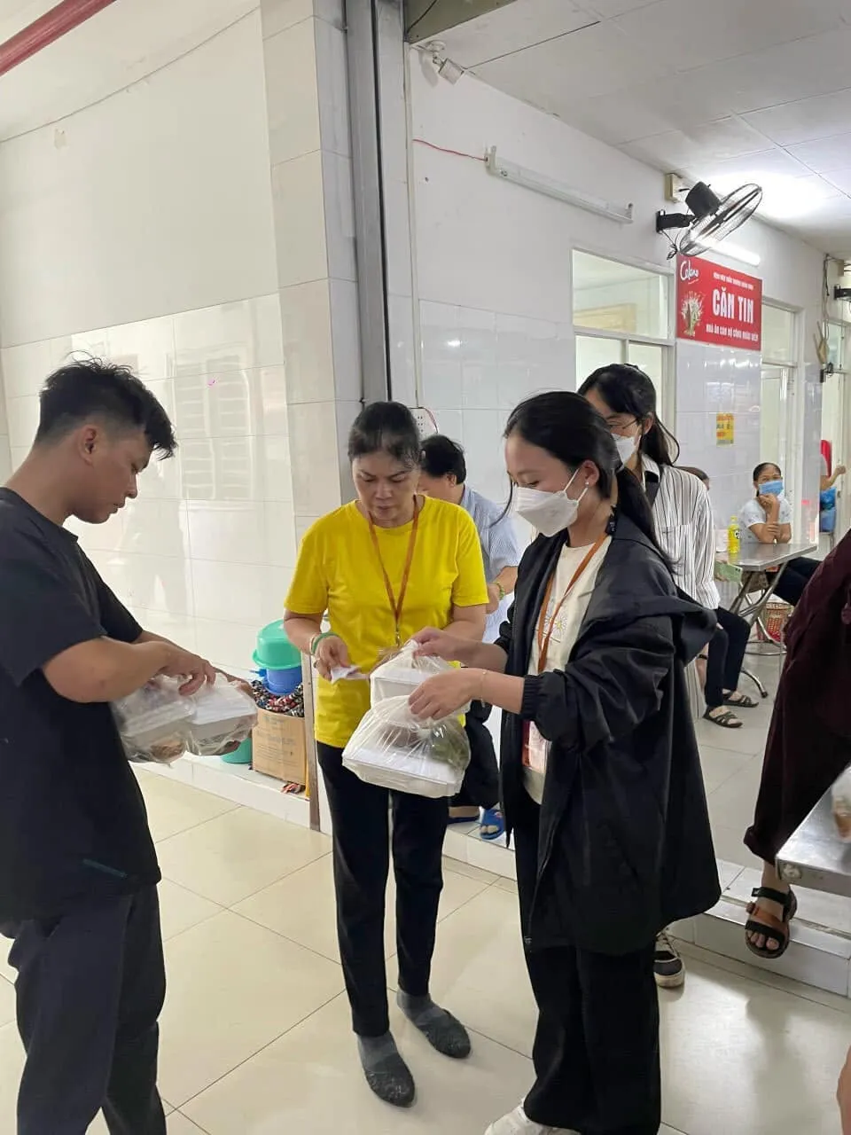 两位志愿者在医院走廊把一袋餐食递给一位年轻人