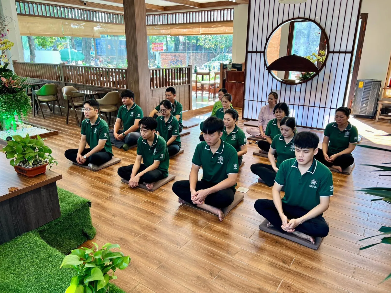 Những người tham dự mặc áo xanh ngồi thiền trên sàn gỗ