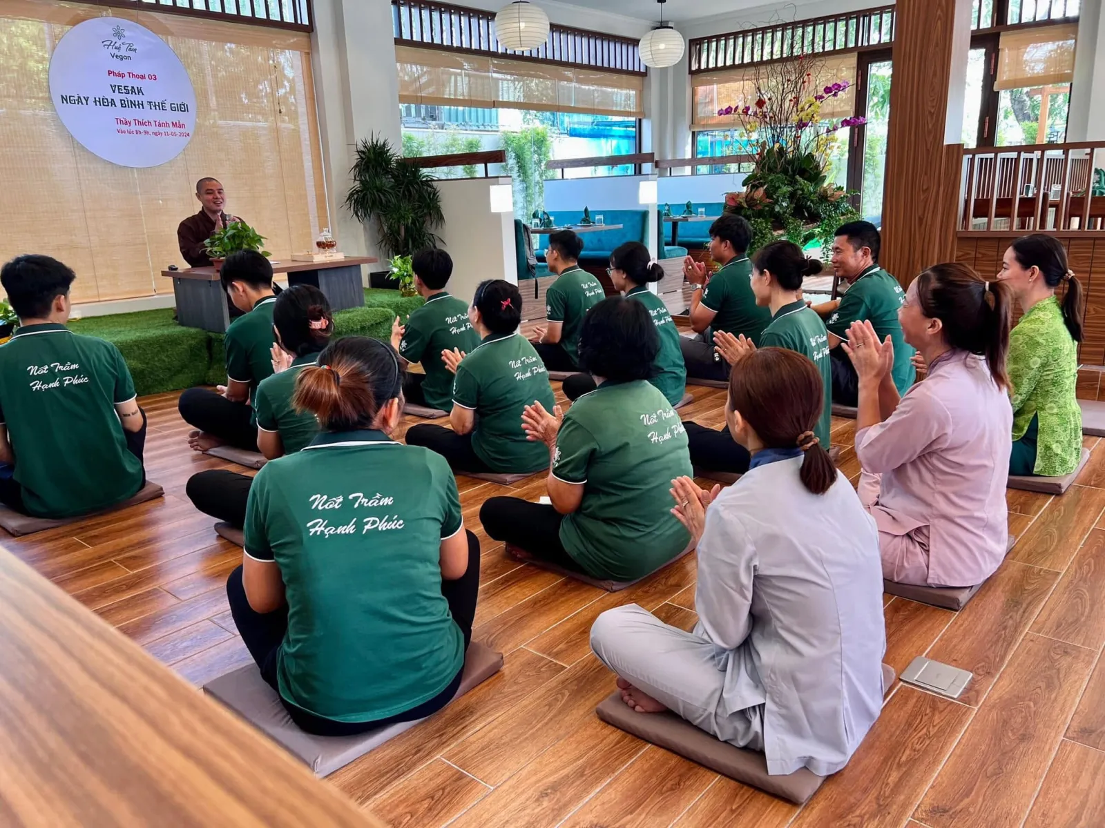 Đại chúng vỗ tay hướng về Thầy, trên lưng áo in chữ “Nốt Trầm Hạnh Phúc”